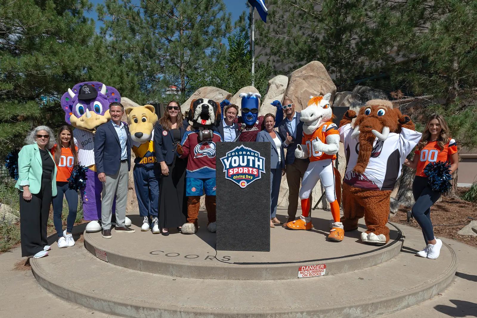 Speakers and mascots pose for a picture at the podium for Colorado Youth Sports Giving Day