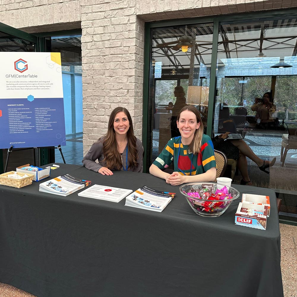 Lauren Noser and Sarah Wool sitting at GFM|CenterTable's information table at the Colorado Nonprofit Association's conference in 2023