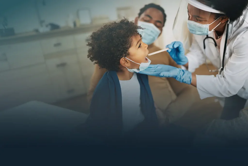 A child gets his mouth examined by a doctor during a checkup while his parent watches