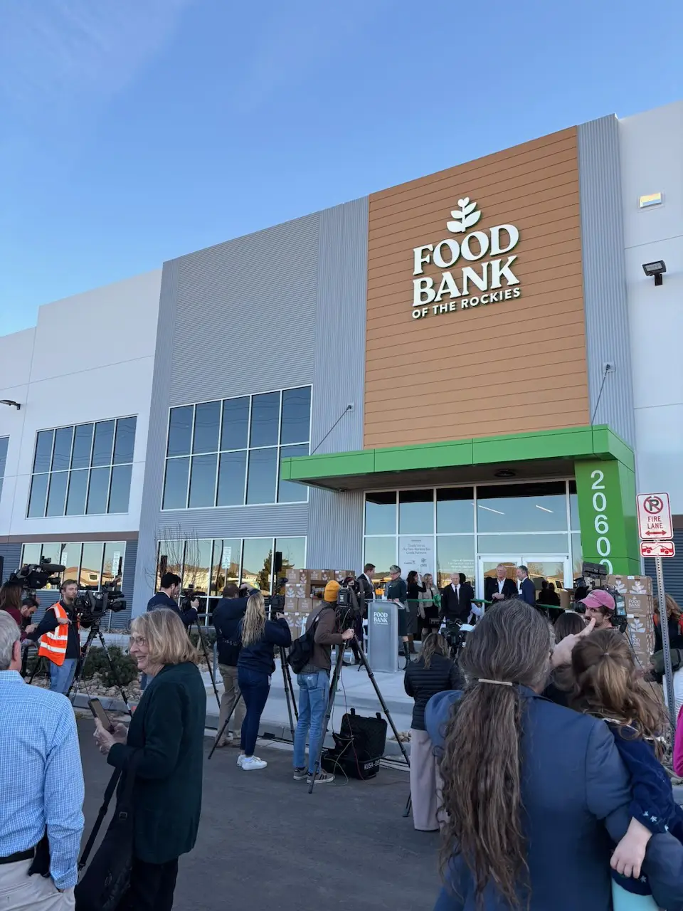A wide shot of the front of a new Food Bank of the Rockies building with media members outside for a grand opening event
